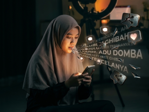 Ilustrasi muslimah menggunakan smartphone dengan efek visual kata ghibah dan adu domba yang keluar dari layar sebagai peringatan bahaya lisan di media sosial.