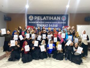 Foto bersama para peserta wanita dan pria memegang sertifikat kelulusan dalam ujian instruktur dansa tingkat dasar ILDI Kabupaten Banyumas di depan spanduk kegiatan.