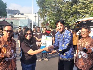 Staf Ahli Bupati Banyumas Arif Triyanto menyerahkan dokumen pelepasan kepada Ketua LPPD Banyumas Pendeta Febe Rustini di halaman Pendopo Si Panji, berlatar belakang bus kontingen dan anggota tim.