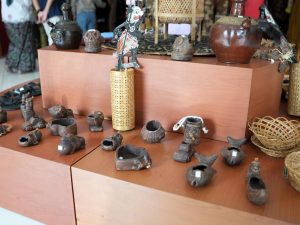 Berbagai produk kerajinan tangan lokal seperti anyaman bambu, wayang, dan gerabah tanah liat dipajang di rak kayu galeri UMKM Griya Kriya Dekranasda Banyumas.