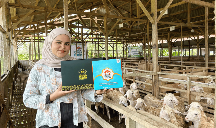 Perwakilan Oemah Aqiqah memperlihatkan dua kemasan paket aqiqah praktis dengan latar belakang kandang domba modern di Banyumas.