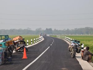 Kondisi jalan aspal mulus di tepi sawah Sumpiuh Banyumas dengan deretan pedagang di pinggir jalan.