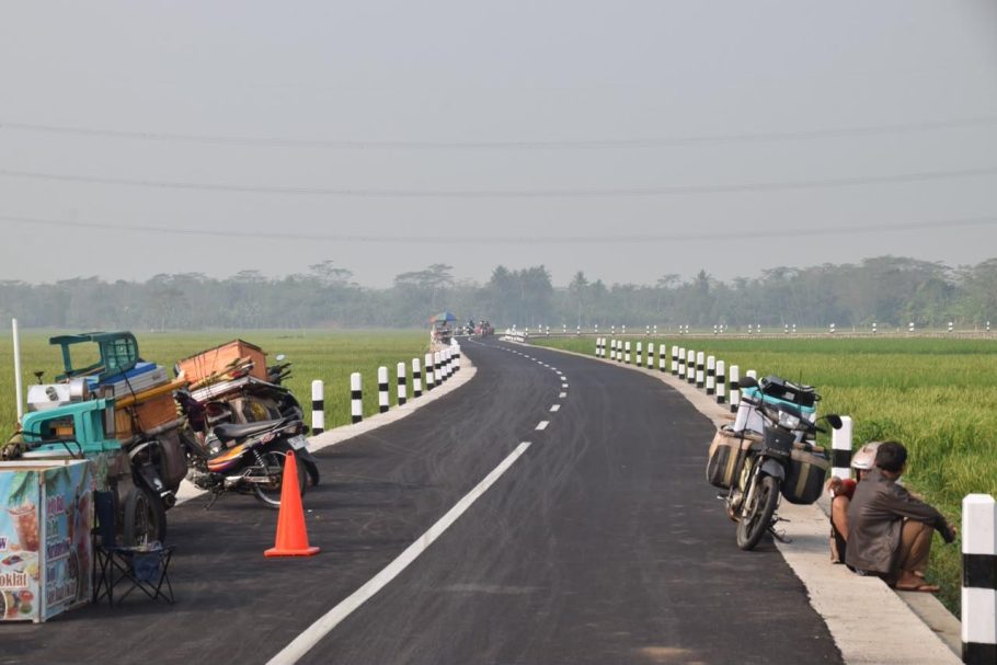 Kondisi jalan aspal mulus di tepi sawah Sumpiuh Banyumas dengan deretan pedagang di pinggir jalan.