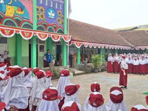 Suasana upacara bendera di halaman SD Negeri 2 Dukuhwaluh Banyumas dipimpin pembina upacara berjas almamater biru di depan barisan siswa seragam merah putih.