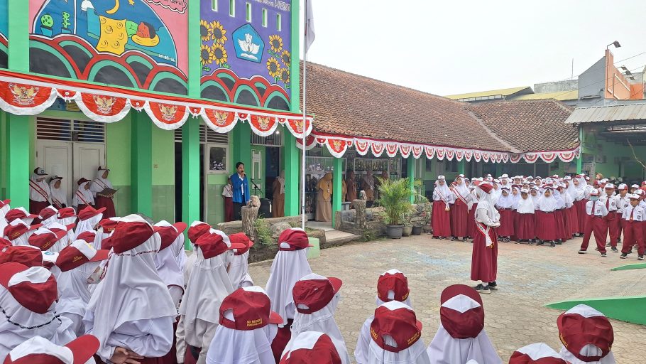 Suasana upacara bendera di halaman SD Negeri 2 Dukuhwaluh Banyumas dipimpin pembina upacara berjas almamater biru di depan barisan siswa seragam merah putih.