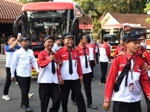 Pengemudi dan petugas Trans Banyumas tersenyum berjalan di depan bus merah saat acara tasyakuran di Pendopo Si Panji