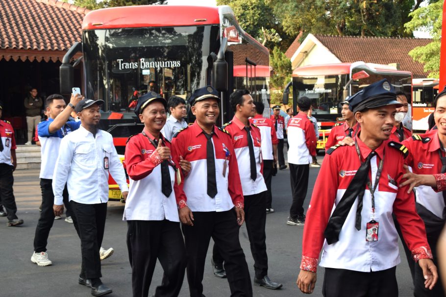 Pengemudi dan petugas Trans Banyumas tersenyum berjalan di depan bus merah saat acara tasyakuran di Pendopo Si Panji